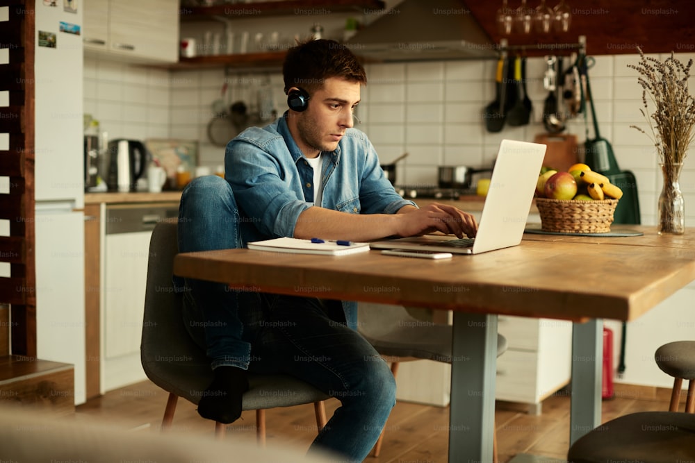 Trabalhador freelancer usando fone de ouvido e trabalhando em um computador em casa.