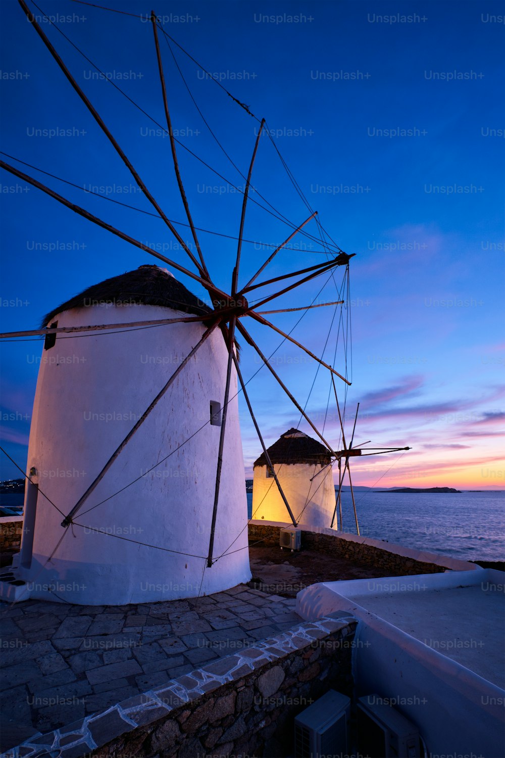 Malerische Aussicht auf die berühmten Windmühlen der Stadt Mykonos Chora. Traditionelle griechische Windmühlen auf der Insel Mykonos, die abends beleuchtet werden, Kykladen, Griechenland. Gehen mit Steadycam.