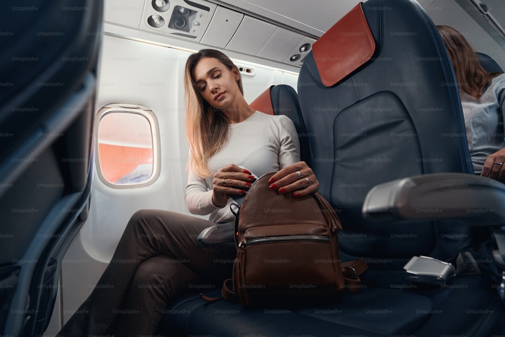 Femmina sul sedile vicino al finestrino che rimette il telefono nella borsa accanto a lei mentre è seduta all'interno della cabina dell'aereo