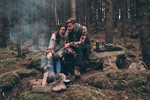 Hermosa pareja joven asando malvaviscos sobre una fogata mientras está sentada en el bosque
