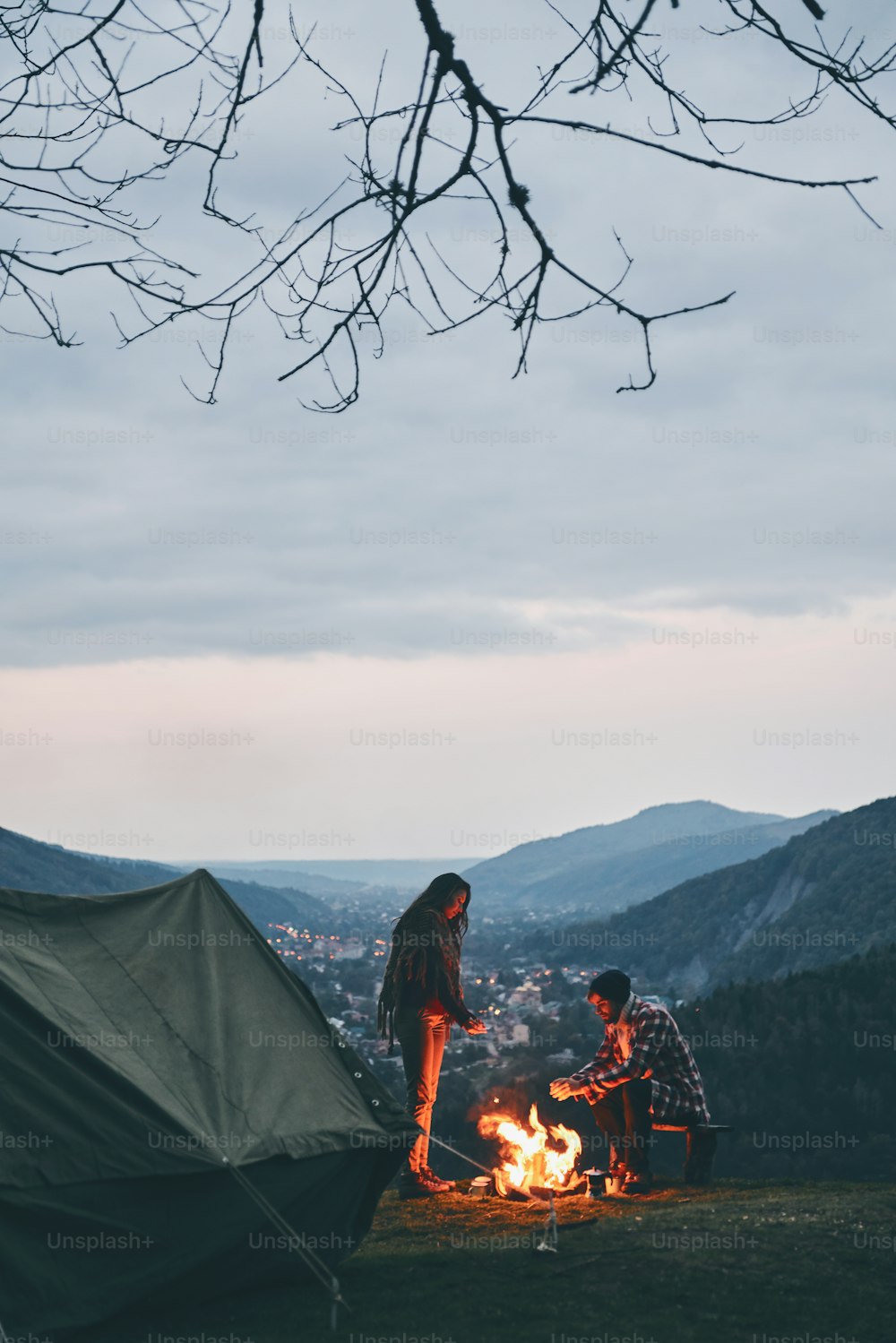 Belo casal jovem aquecendo-se pela fogueira enquanto acampa nas montanhas