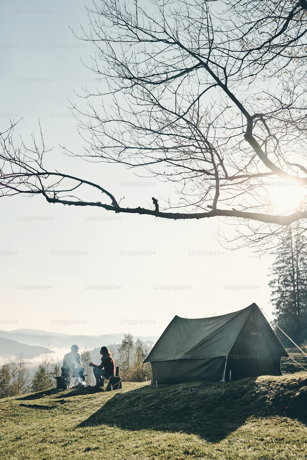 Young couple having morning coffee while sitting near the tent in mountains