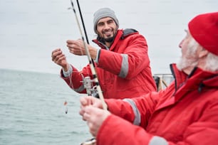 Professional fishing. Waist up portrait view of the unshaven young man telling something to his senior colleague while preparing to the fishing. Stock photo