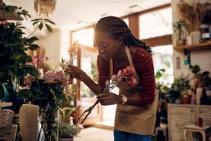 Jeune femme afro-américaine appréciant tout en faisant des arrangements floraux et en travaillant dans son magasin de fleurs.