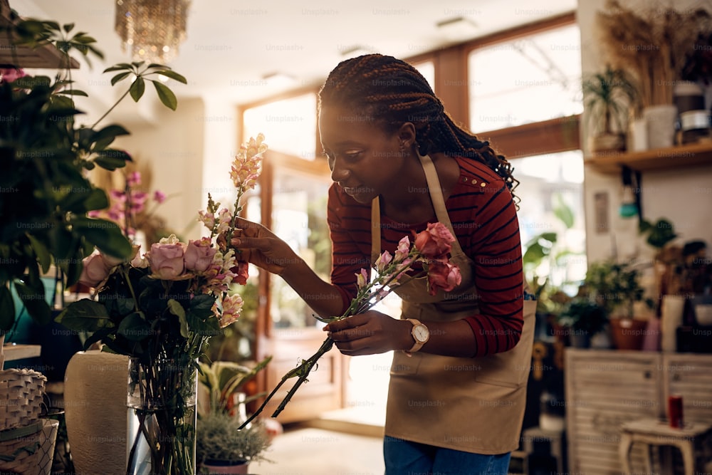 Young African American woman enjoying while making flower arrangement and working at her flower shop.