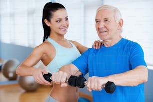 Confident female physical therapist helping senior man with fitness in health club