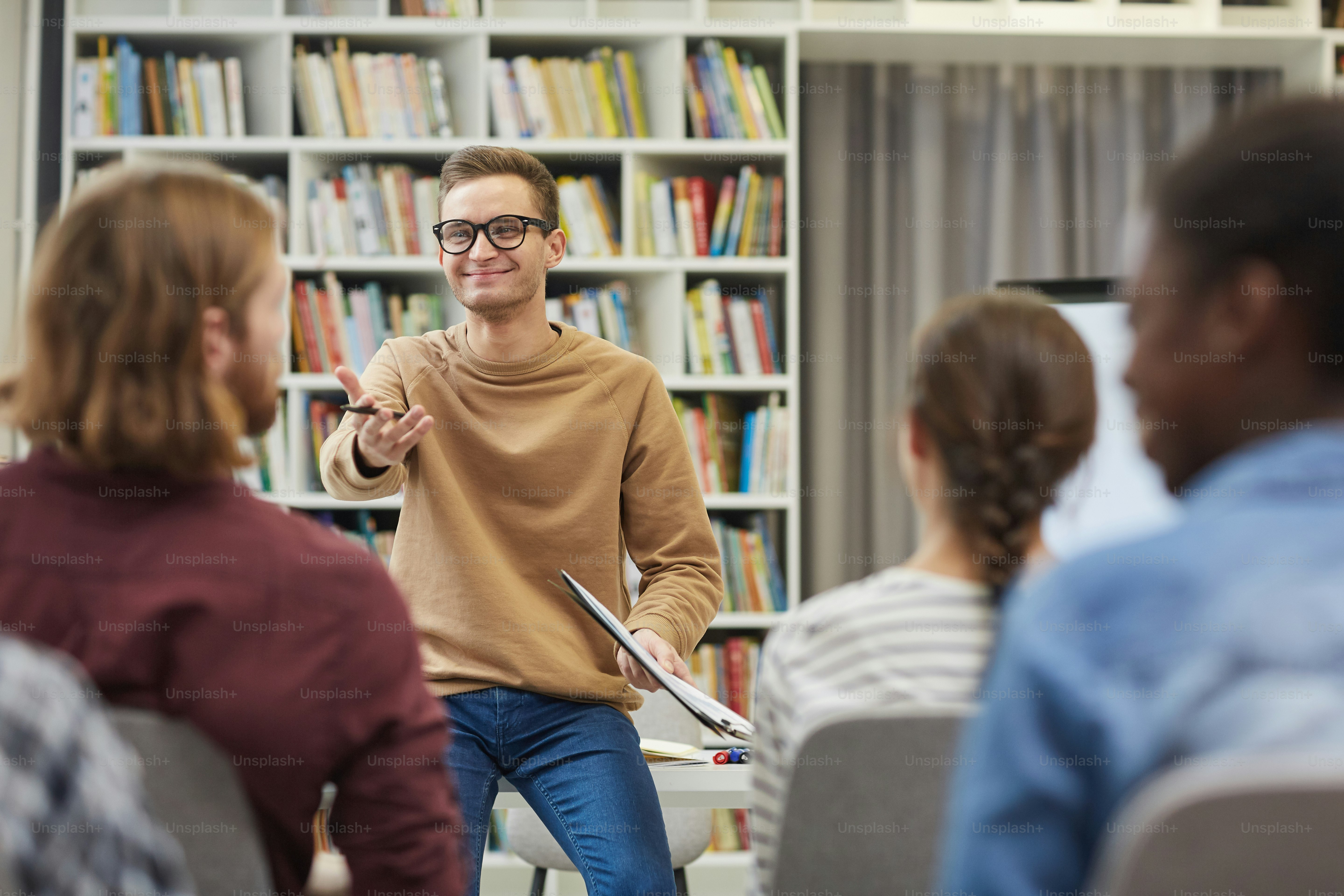 Young speaker in eyeglasses speaking with young people during business training