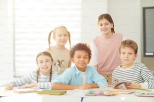 Portrait of smart boys and girls sitting and standing together in modern classroom looking at camera, horizontal shot, copy space