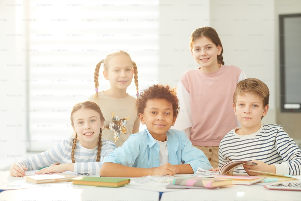 Retrato de meninos e meninas inteligentes sentados e em pé juntos na sala de aula moderna olhando para a câmera, tiro horizontal, espaço de cópia