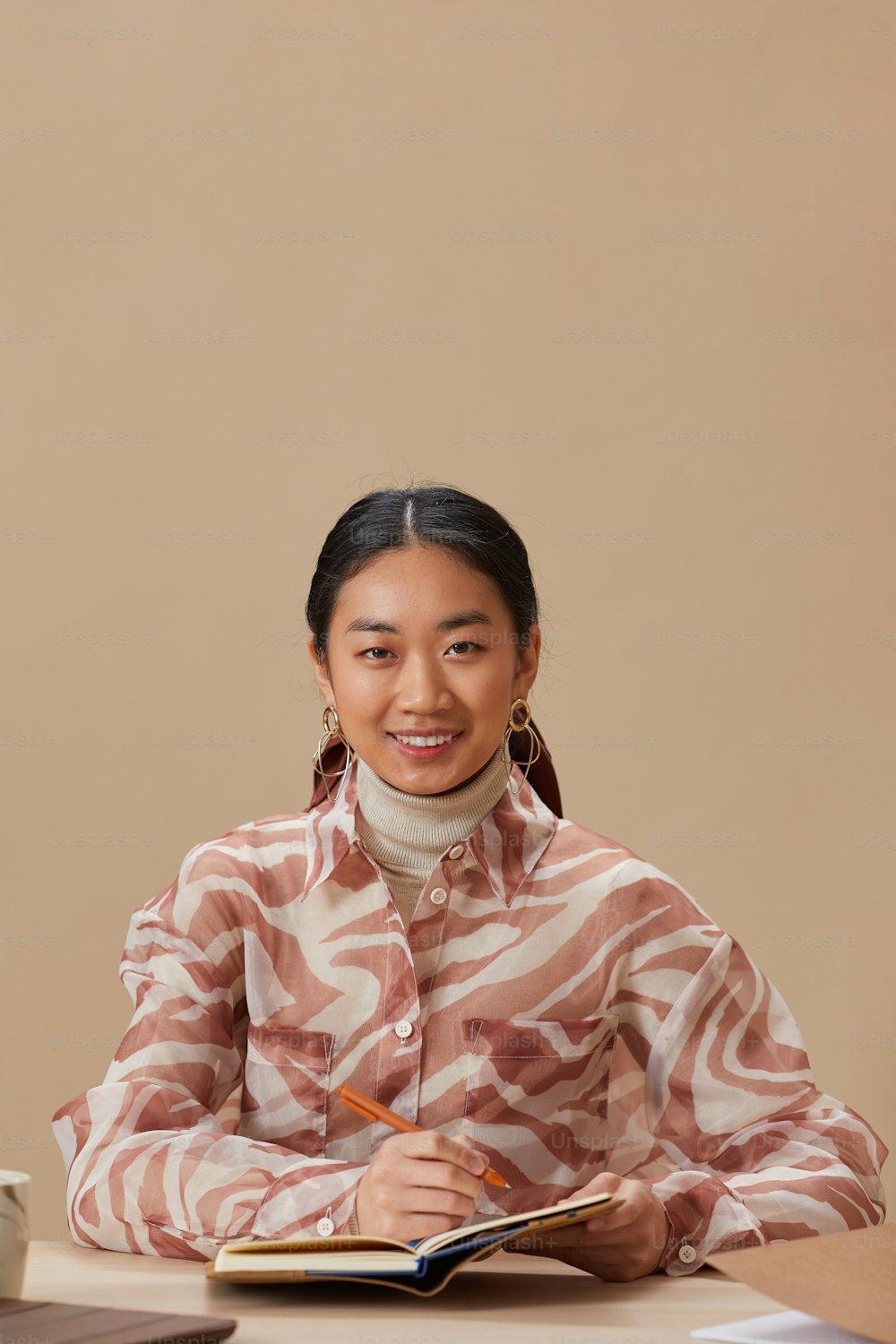 テーブルに座ってメモ帳に書きながらカメラで微笑む若いアジア人女性の肖�像画