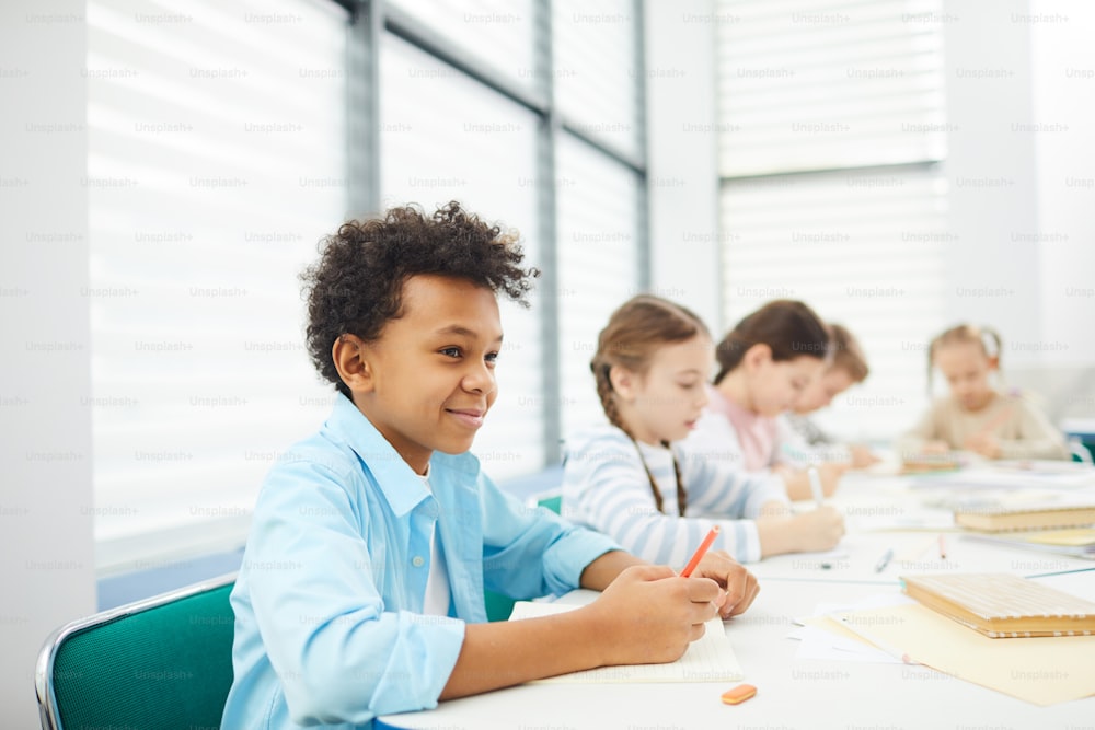 Ritratto orizzontale di cinque bambini che indossano abiti casual seduti alla scrivania in aula moderna che lavorano sul compito, spazio di copia