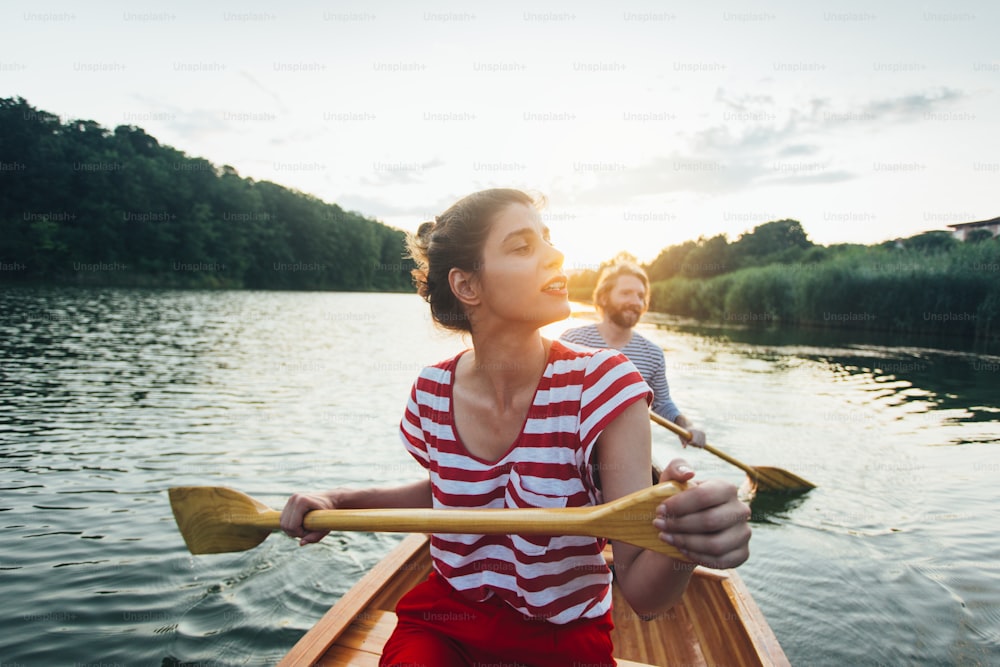 Mujer joven remando en canoa con novio en el lago de la puesta del sol.