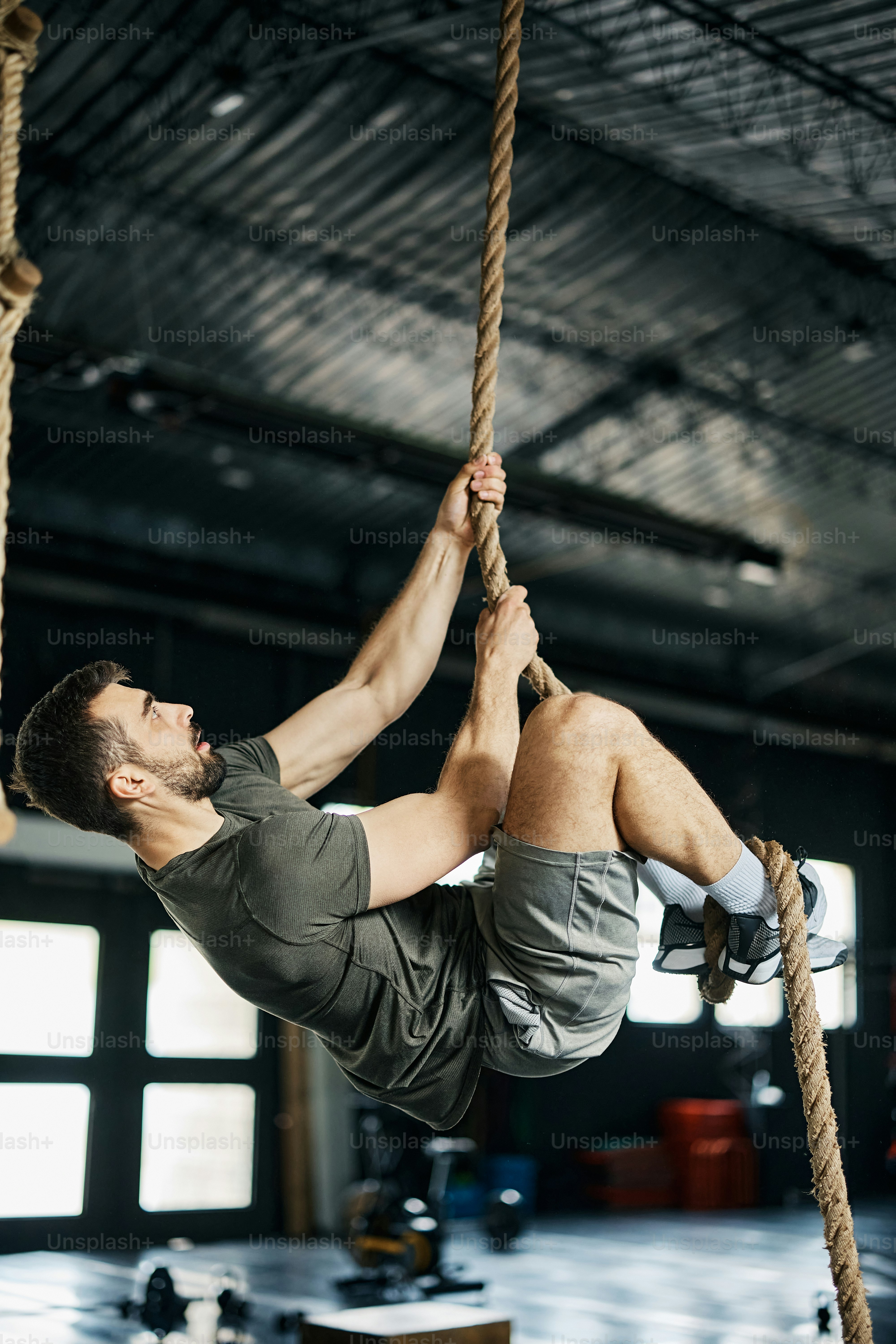 Athletic man climbing up the rope during cross training in a gym. photo ...