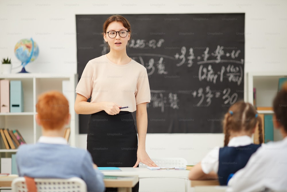 眼鏡をかけた若い女性が学校で教師として働き、学童に教えている
