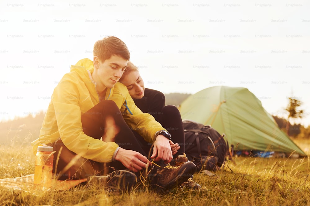 Young lovely couple sitting near tent outdoors at daytime. Beautiful sunlight.