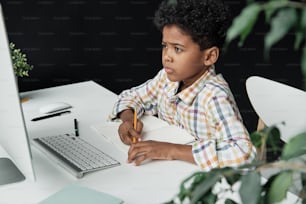 Little boy sitting at the table and looking at computer monitor he studying at home