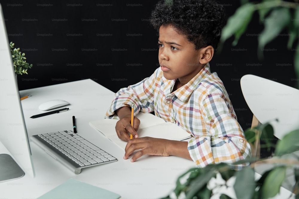 Little boy sitting at the table and looking at computer monitor he studying at home