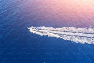 Boat launch at high speed floats to sunlight in the ocrean, aerial top view