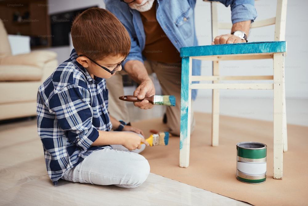 おじいさんと一緒に家具を修理したり、木製の椅子を青く塗ったりする小さな男の子。