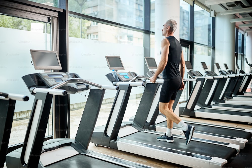 Mature athlete warming up for sports training and walking on treadmill in a gym.
