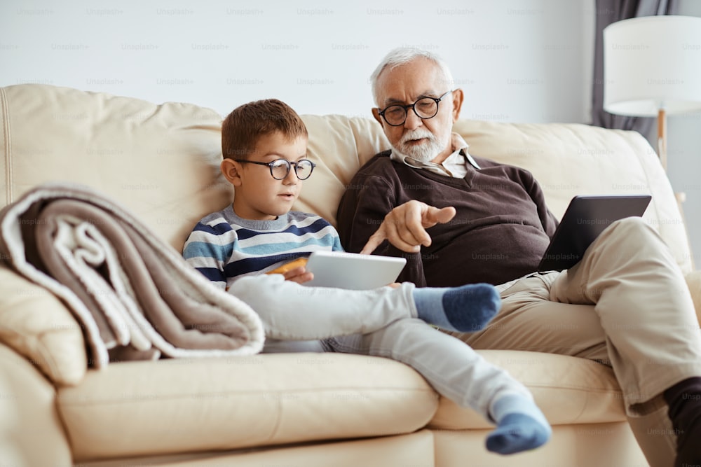 Small boy and his grandfather using digital tablet on the sofa at home.