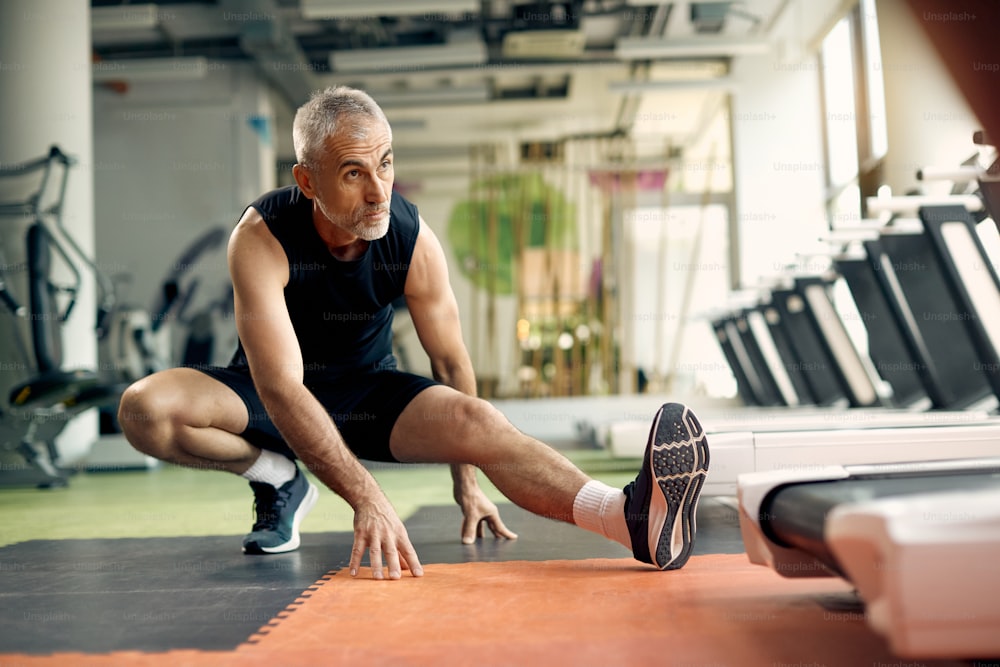 Mature athlete stretching his legs before sports training in a gym.