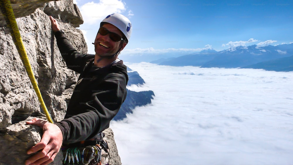 guía de montaña masculino sonriendo en una empinada escalada vertical en roca en un entorno magnífico por encima de un mar de nubes en el valle de abajo en los Alpes suizos cerca de Coira