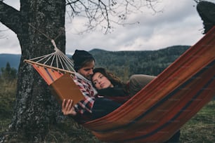 彼氏とハンモックに横たわりながら本を読んでいる美しい若い女性