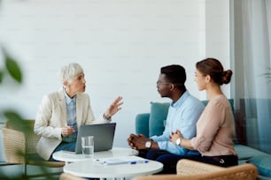 Un agent d’assurance mature et un couple multiracial discutent lors d’une réunion au bureau.