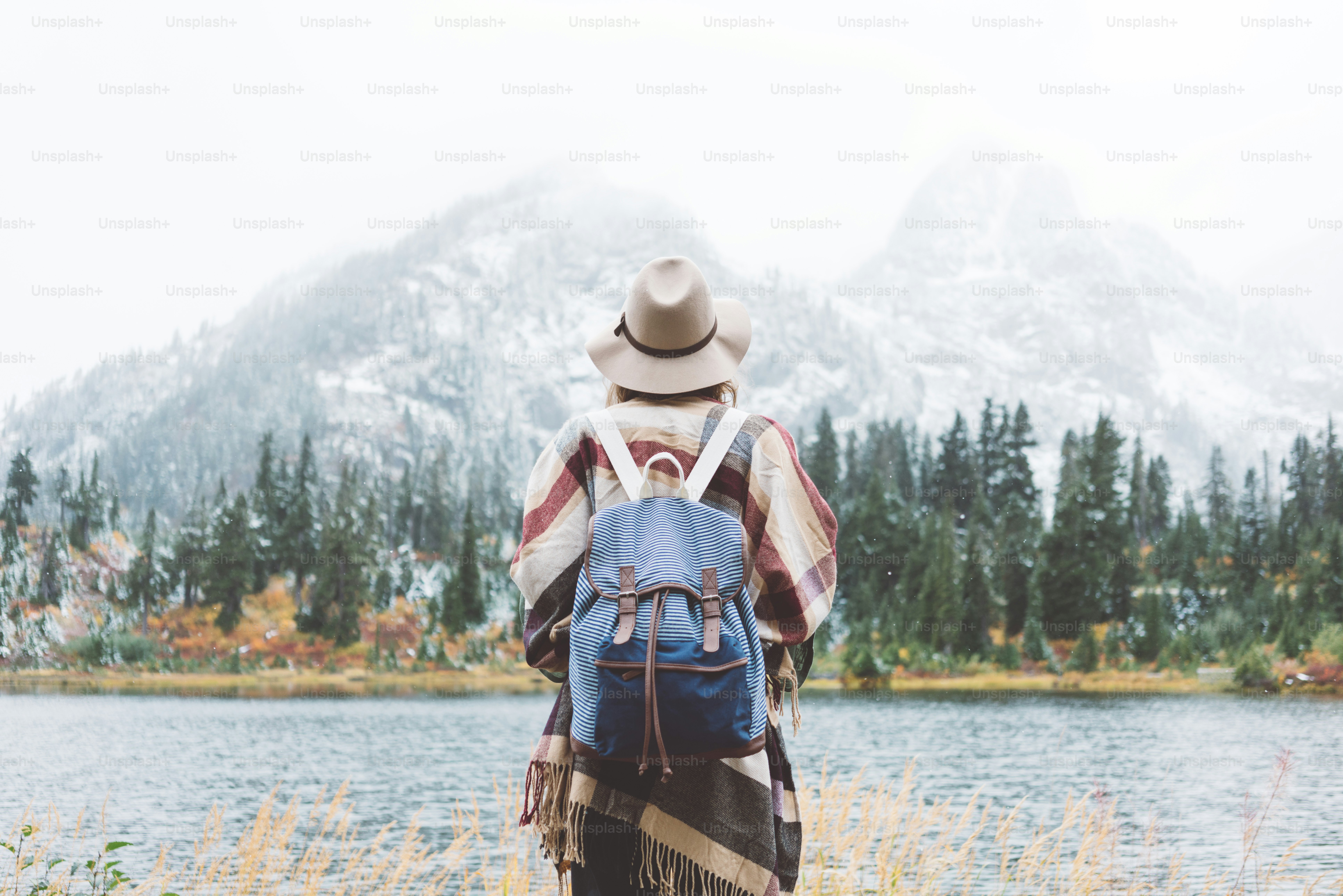 Donna stiginosa che si sente felice tra montagne incredibili, goditi la natura landsape. Foresta e lago, zaino in spalla, cappello e poncho, stile boho e voglia di viaggiare