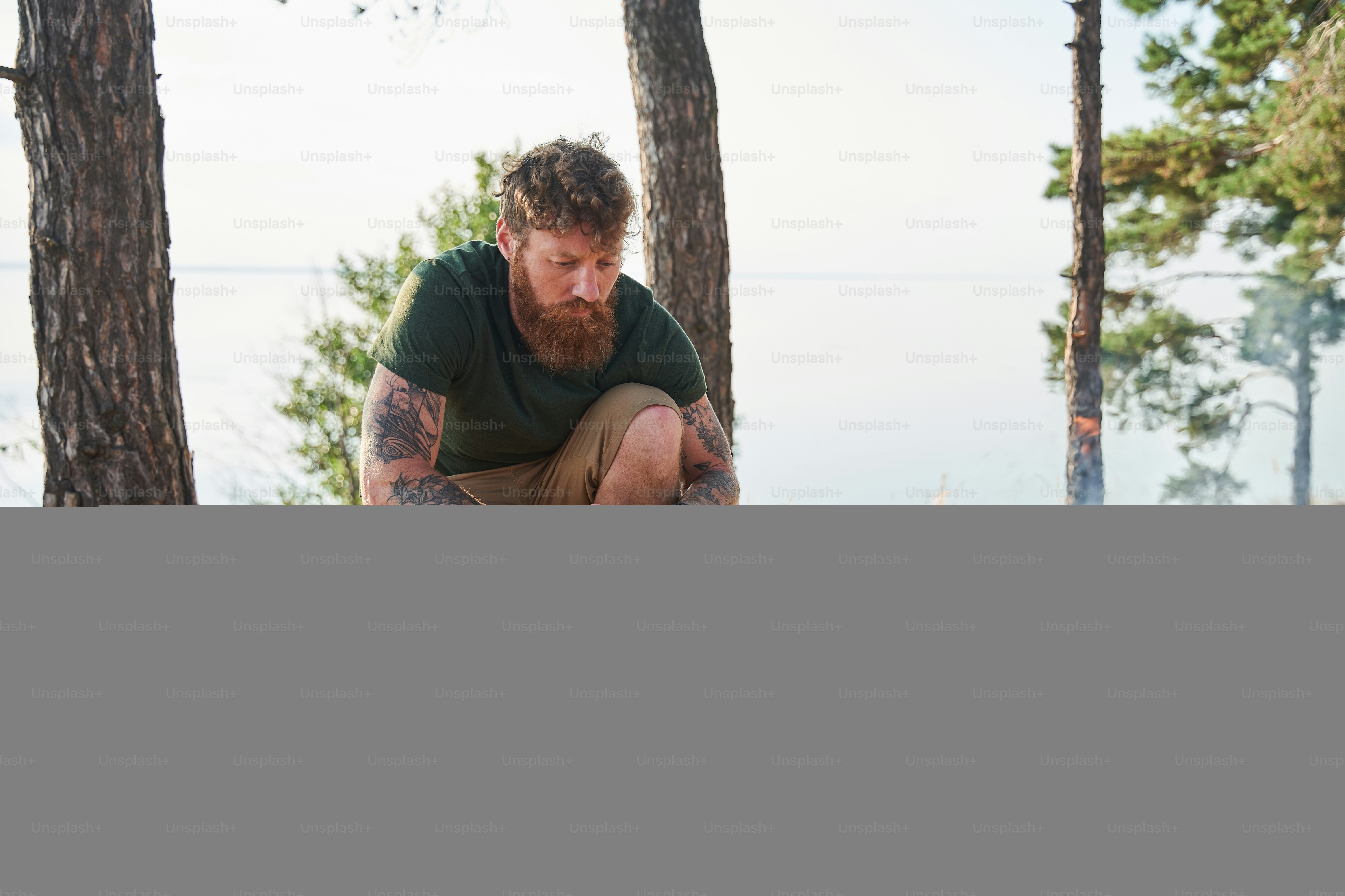 Outdoor sweet. Full length view of the bearded man frying marshmallows at the forest near the campfire. His daughter sitting at the blanket