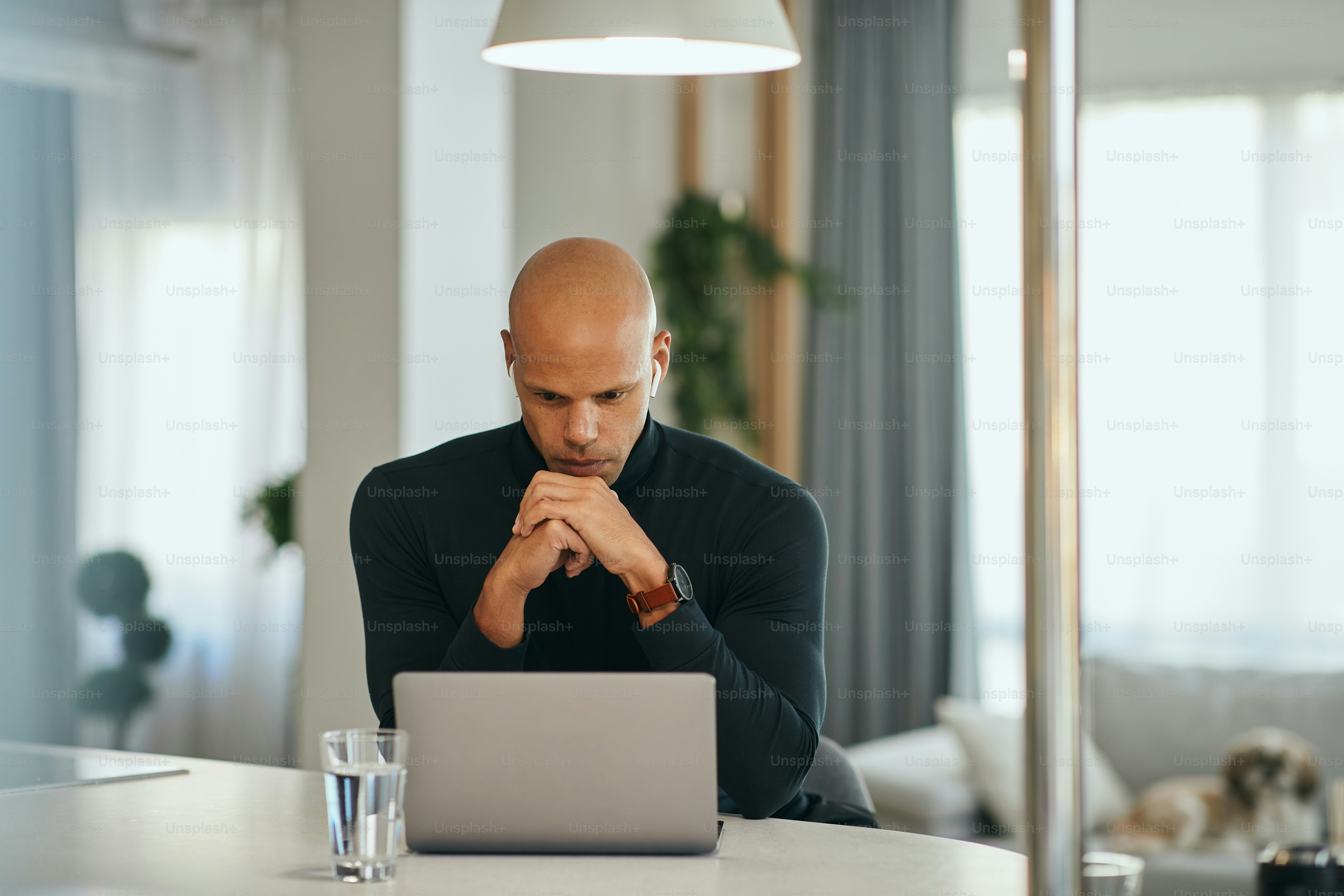 Young African American businessman reading problematic e-mail on laptop while working at home office.