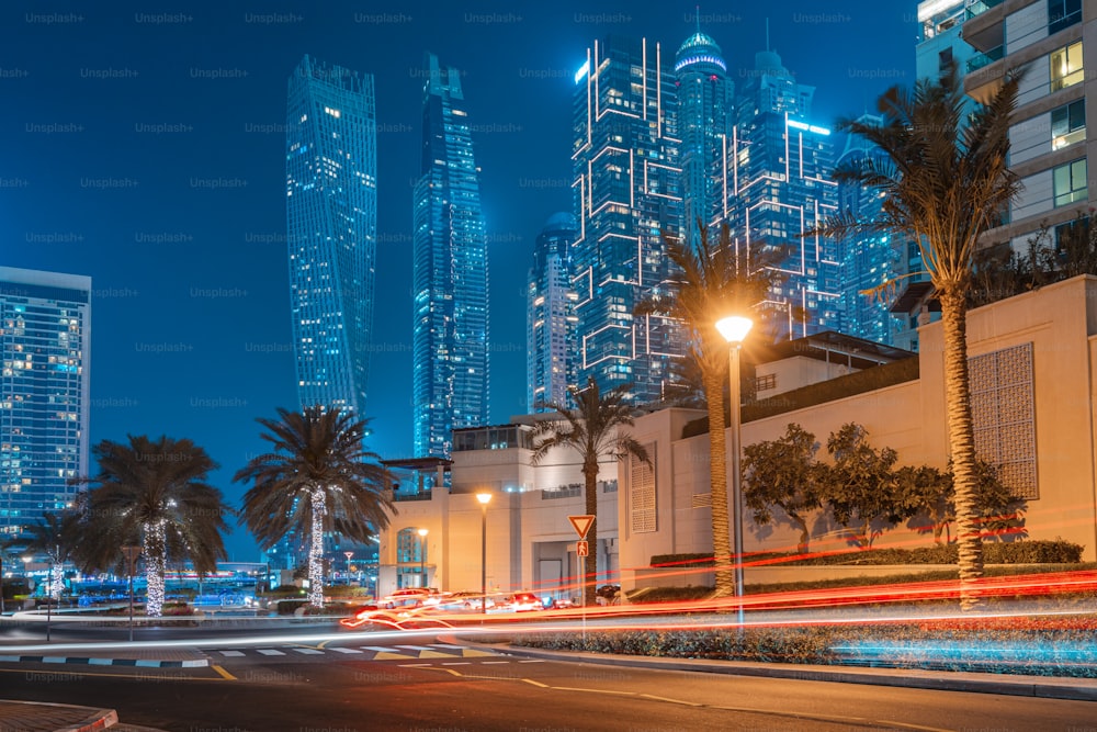 A photo with a long exposure with visible traces from the headlights of passing cars and illuminated skyscrapers in the Dubai Marina district