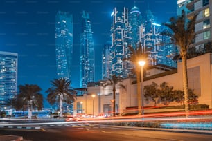 A photo with a long exposure with visible traces from the headlights of passing cars and illuminated skyscrapers in the Dubai Marina district