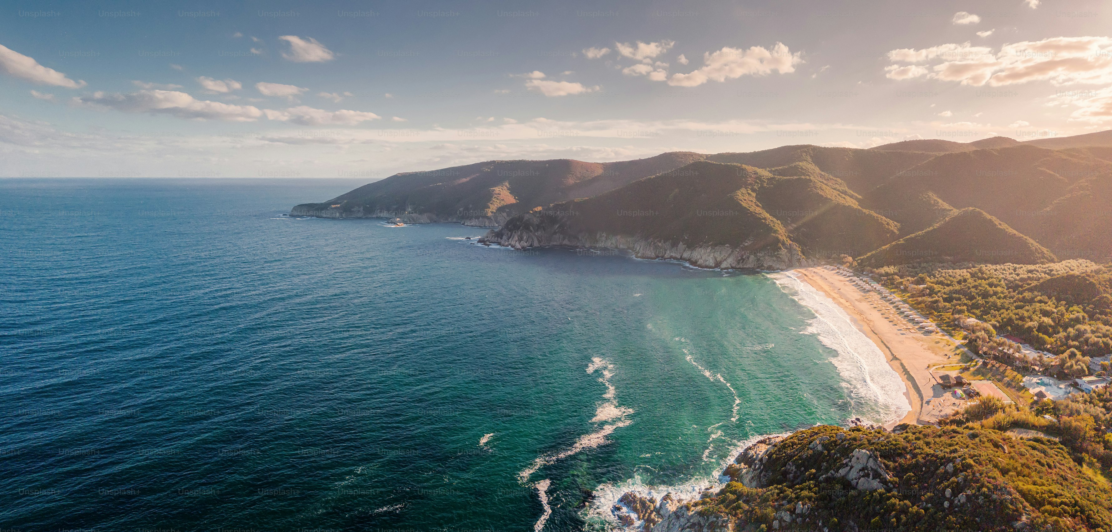 Aerial view of a sandy beach along a coastline with green hills at golden hour
