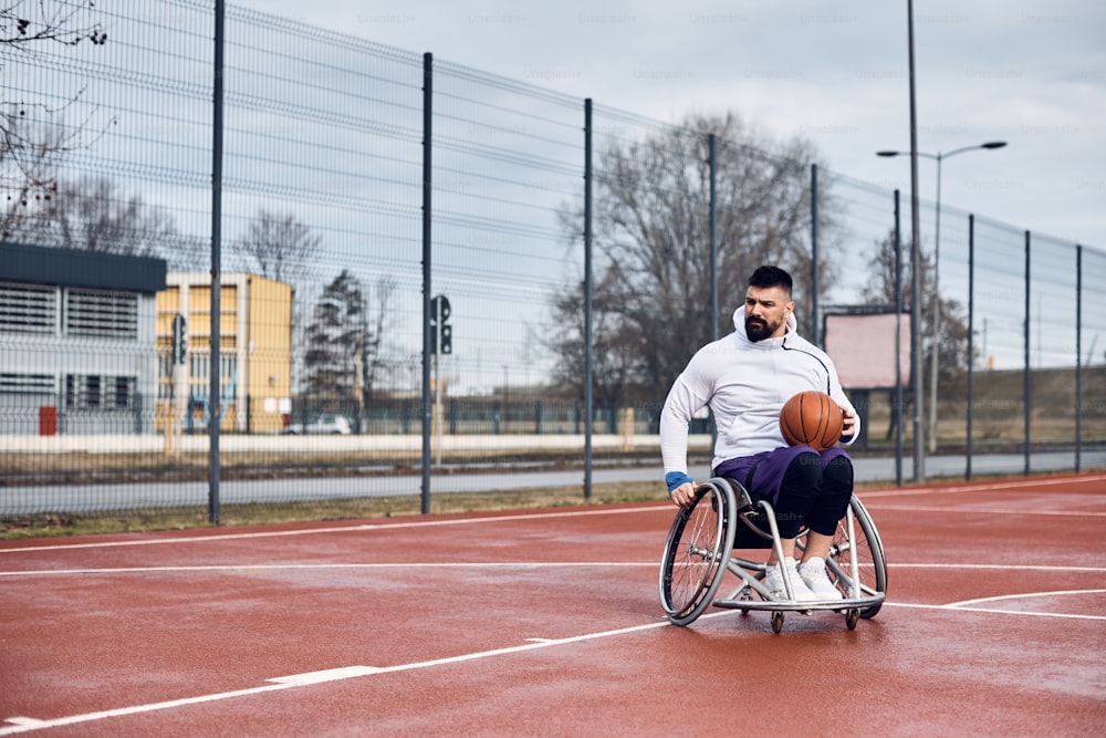 Young basketball player in wheelchair on outdoor sports court. Copy space.