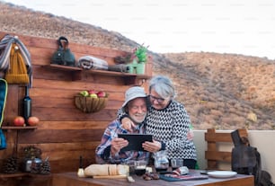 Fröhliches älteres Paar umarmte den Blick auf den Laptop. Nach dem Wandern machen sie eine Pause. Holztisch mit Käse, Salami und Rotwein.