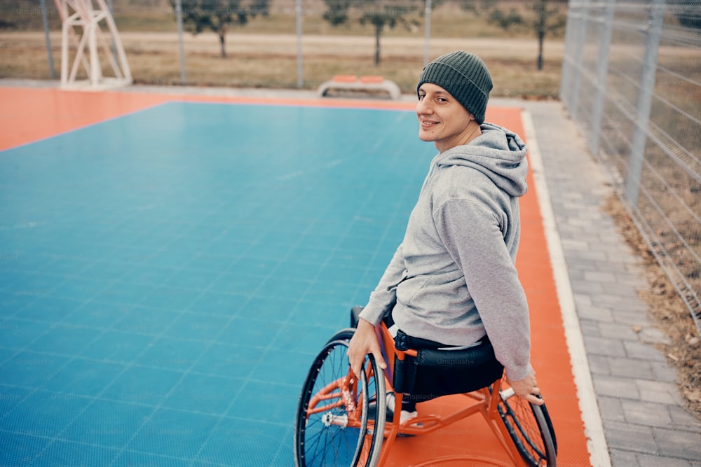 Young man with disability warming up before basketball training on outdoor court. Copy space.
