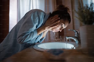 Giovane donna che si lava il viso in bagno di notte.