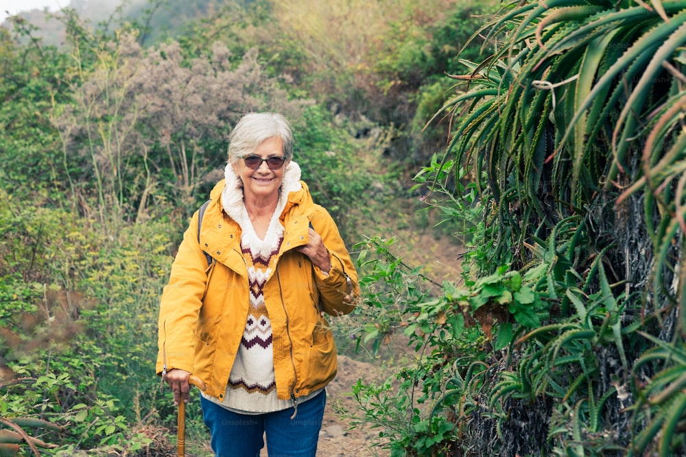 Smiling senior woman outdoor on mountain excursion wearing winter sweater and yellow jacket. Relaxed elderly woman enjoying freedom and nature