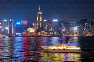 Paesaggio urbano dello skyline di Hong Kong grattacieli del centro sopra Victoria Harbour la sera illuminati con traghetti turistici in barca. Hong Kong, Cina
