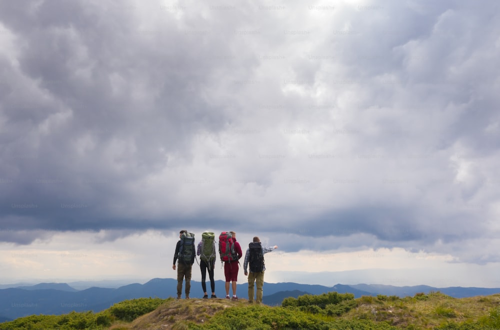 As quatro pessoas com mochilas de pé na montanha contra belas nuvens