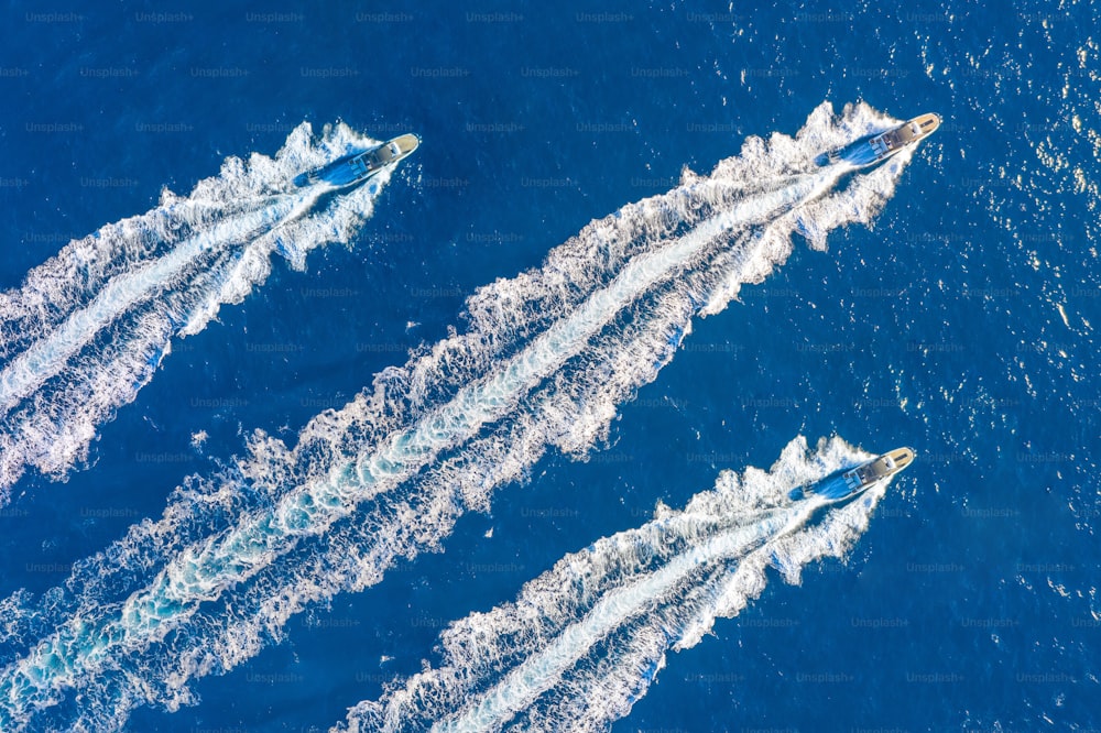 Three speed boats launch at high speed floats in the ocean, aerial top view