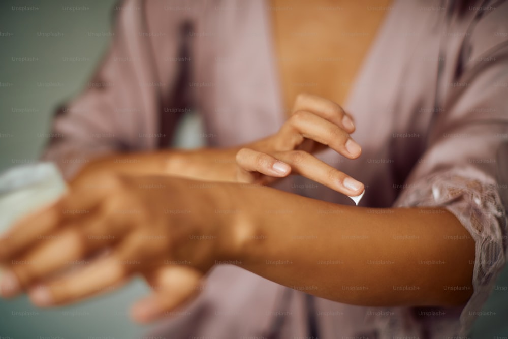 Primer plano de una mujer cuidando su piel y aplicándose crema corporal en los brazos.