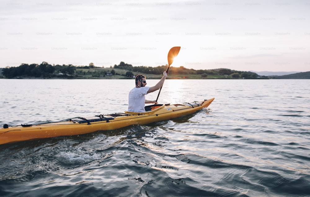 Man kayaker paddling the kayak at sunset lake.