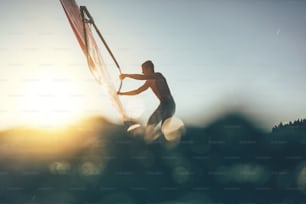 Niedrige Winkelansicht der Surfersilhouette, die auf dem Windsurfbrett balanciert. Windsurfer segeln auf dem Windsurfbrett.