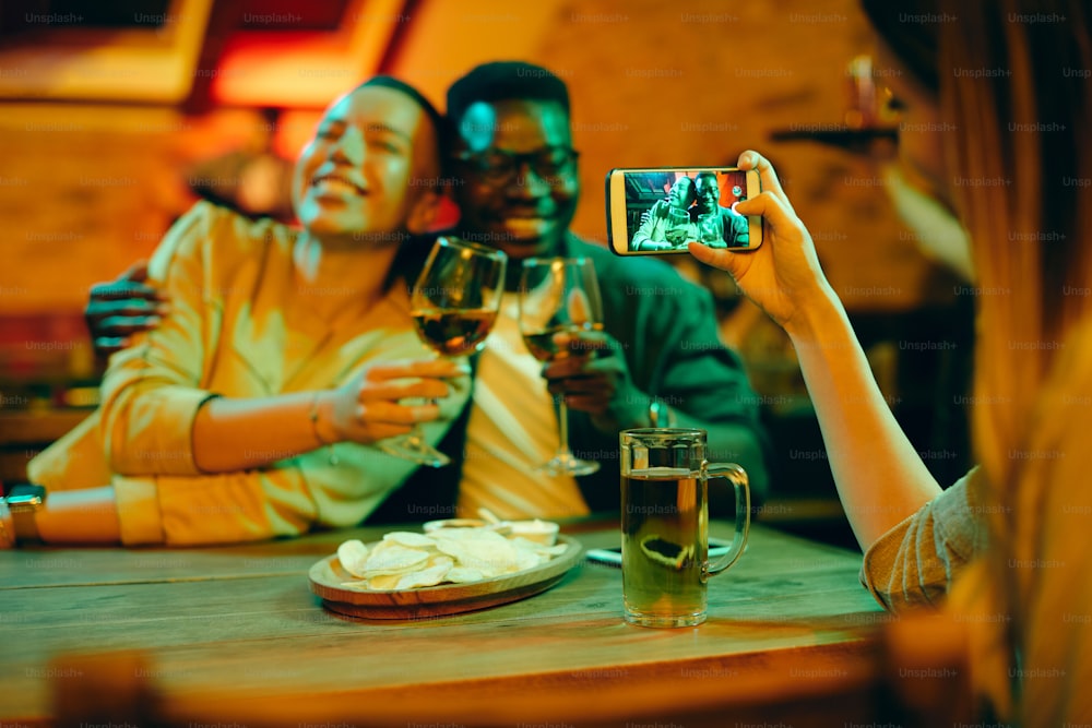 Close-up of woman taking picture of African American couple during their night out in a bar.