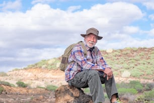 Retrato de un anciano barbudo que lleva una mochila mientras descansa mirando la montaña y sonriendo. Anciano en forma en un viaje de senderismo disfrutando de la libertad de la aventura y unas vacaciones saludables