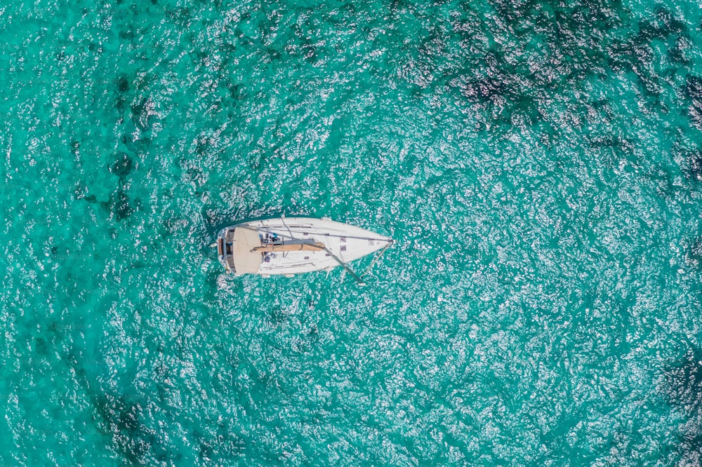 Yacht bianco in una laguna con acqua lucida azzurra, vista aerea dall'alto