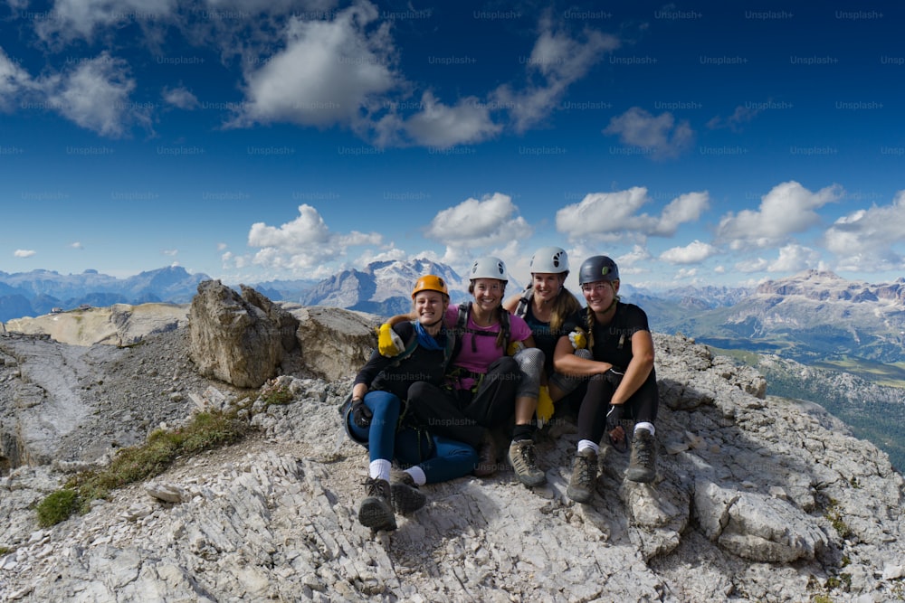 Cuatro atractivas alpinistas se abrazan y sonríen en la cima de una montaña después de una dura escalada en los Dolomitas italianos cerca de Cortina d'Ampezzo
